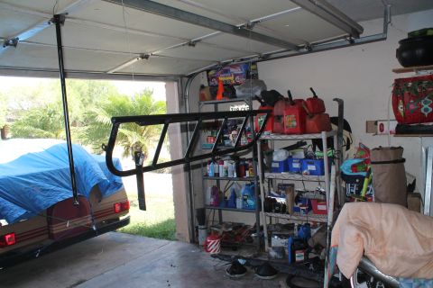 1990 Ford Bronco - A roll cage is suspended in a garage, with a tarp-covered vehicle visible outside.