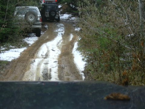 1991 Ford Bronco - Off-road vehicles navigate a challenging muddy and snowy trail through a wooded area.