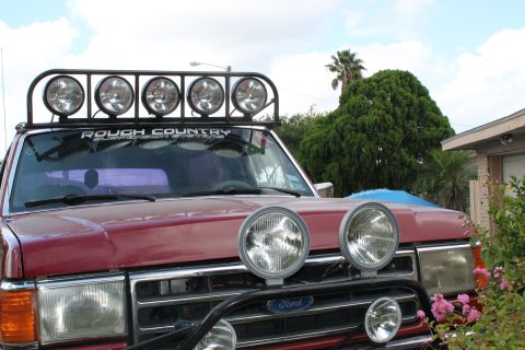 1990 Ford Bronco - Front view of a red Ford Bronco equipped with a light bar and auxiliary lights, parked outdoors.