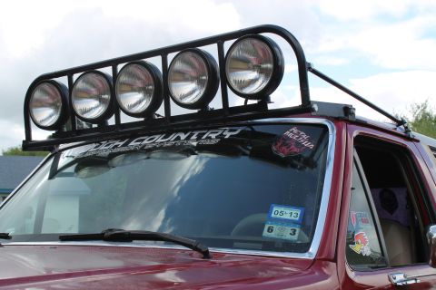 1990 Ford Bronco - This red SUV features a prominent roof-mounted light bar and 'Rough Country' branding on the windshield.