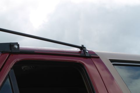 1990 Ford Bronco - A roof rack system is attached to the top of a maroon SUV, with a tan cap visible in the background.