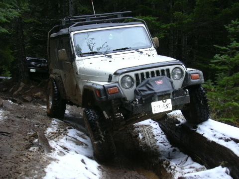 1991 Ford Bronco - A white Jeep Wrangler navigates a challenging off-road trail with snow and mud.