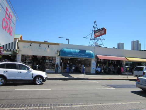 1991 Ford LTD Crown Victoria - A street scene in a commercial area shows various shops and vehicles under a clear blue sky.