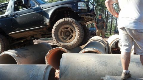 1992 Ford Bronco - A modified truck attempts to drive over a series of large concrete pipes in a wooded area.