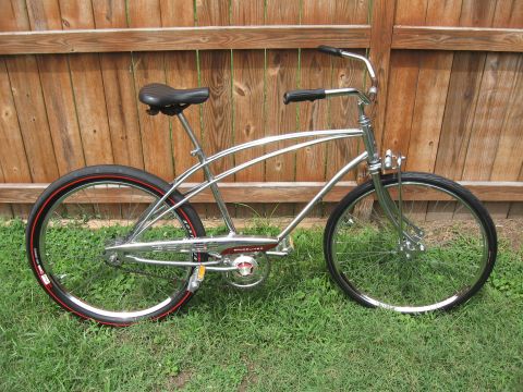 1994 Ford Bronco - A shiny chrome cruiser bicycle with red-striped tires is parked on a grassy lawn in front of a wooden fence.