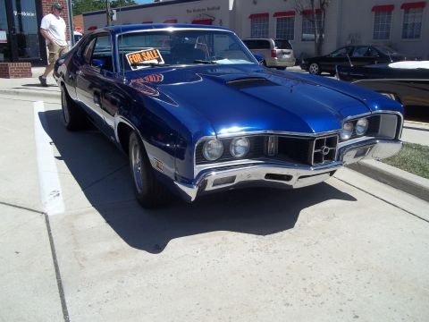 1970 Ford Ranchero - A blue coupe sits on a paved lot with a 'For Sale' sign in the window.