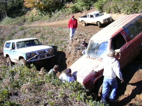 1991 Ford Bronco - Several off-road vehicles are stuck in a muddy ditch on a dirt path.