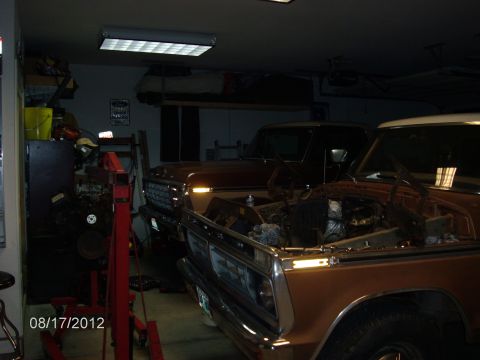 1979 Ford F-150 - Two 1979 Ford F-150 trucks are parked in a garage, with the front truck's hood open, revealing its engine bay.