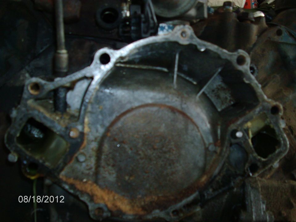 Rusty metal engine timing cover with bolt holes and fluid residue