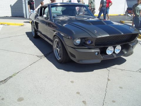 1970 Ford Ranchero - Dark gray 1967 Shelby GT500 Mustang parked on pavement with people in the background.
