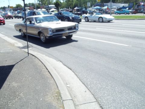 1970 Ford Ranchero - A classic gold Pontiac GTO cruises down a street with other vehicles and tents visible.