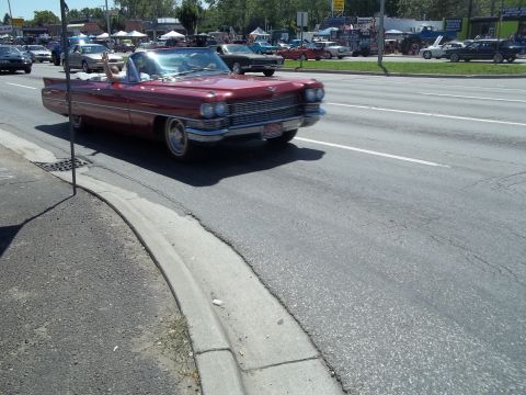 1970 Ford Ranchero - A classic red convertible cruises down the road with other vehicles in the background.
