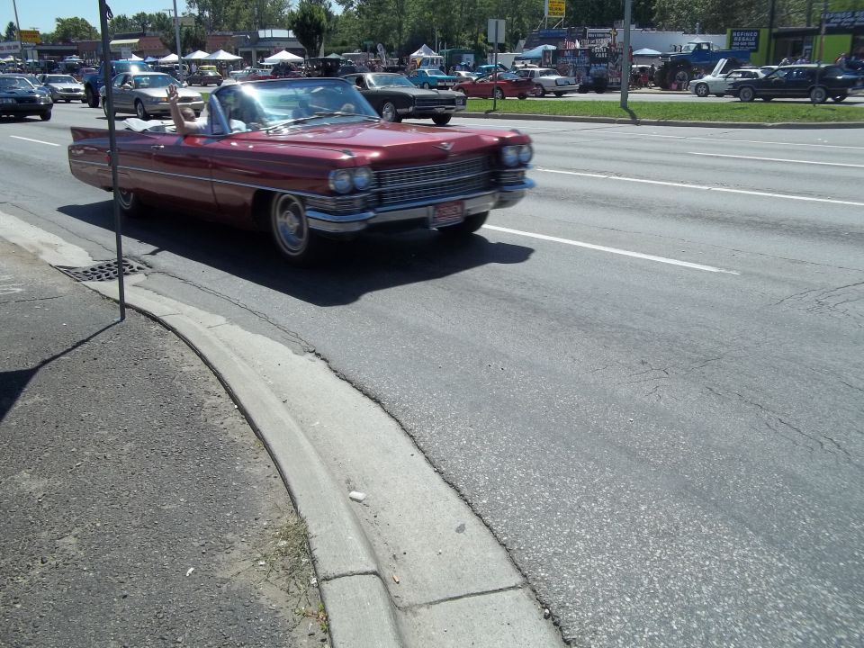 Red convertible with fins and chrome grille driving on a sunny day