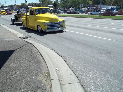 1970 Ford Ranchero - A bright yellow pickup truck from the 1950s tows a trailer down a suburban street.
