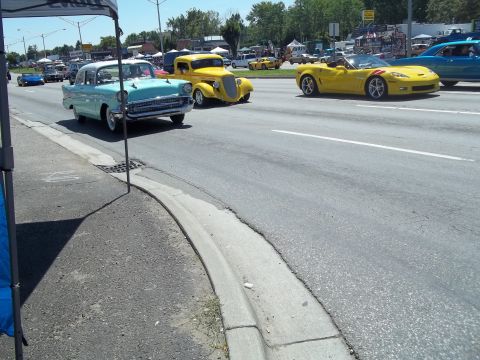 1970 Ford Ranchero - Several classic and modern cars cruise down a street on a bright, sunny day.