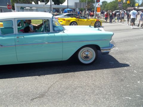 1970 Ford Ranchero - A classic aqua and white 1957 Chevrolet Bel Air sedan is seen from the side, with a modern yellow Corvette driving behind it.