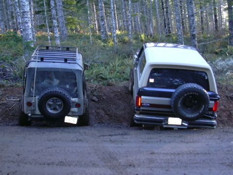 1991 Ford Bronco - Two off-road vehicles, a 1991 Ford Bronco and a Jeep Wrangler, navigate a dirt path in a forest.