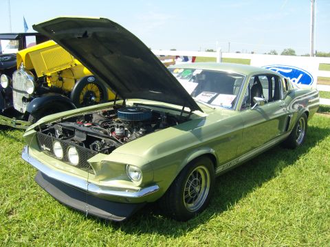 2007 Ford Mustang - A classic Ford Mustang Fastback is displayed with its hood open at an outdoor event, with another vintage vehicle visible behind it.