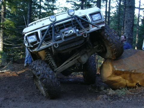 1991 Ford Bronco - This modified Ford truck is navigating a large rock on a wooded trail.