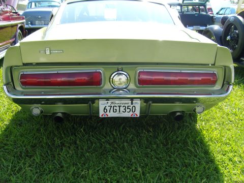 2007 Ford Mustang - The rear view of a classic Mustang shows its iconic taillights and a GT350 badge, parked on grass with other vehicles nearby.
