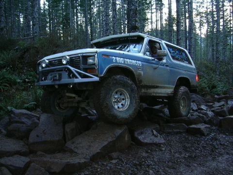 1991 Ford Bronco - A blue Ford Bronco navigates a challenging rocky trail in a forest.