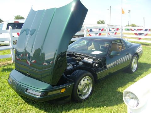 2007 Ford Mustang - Green Corvette with hood open, revealing the engine bay. The car is parked on grass with a white fence in the background.