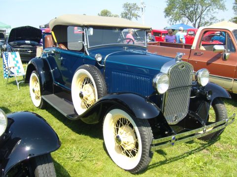 2007 Ford Mustang - A vintage blue convertible with a tan top and white wall tires is parked on grass at an outdoor event.