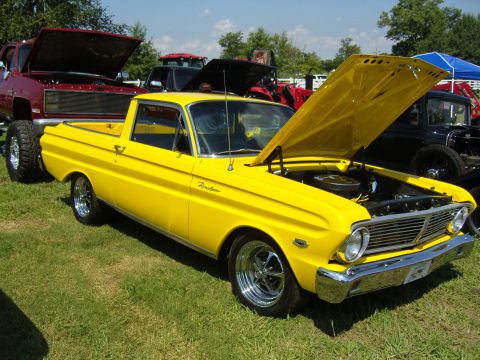 2007 Ford Mustang - A yellow pickup truck is displayed with its hood open, alongside other vehicles on a sunny day.