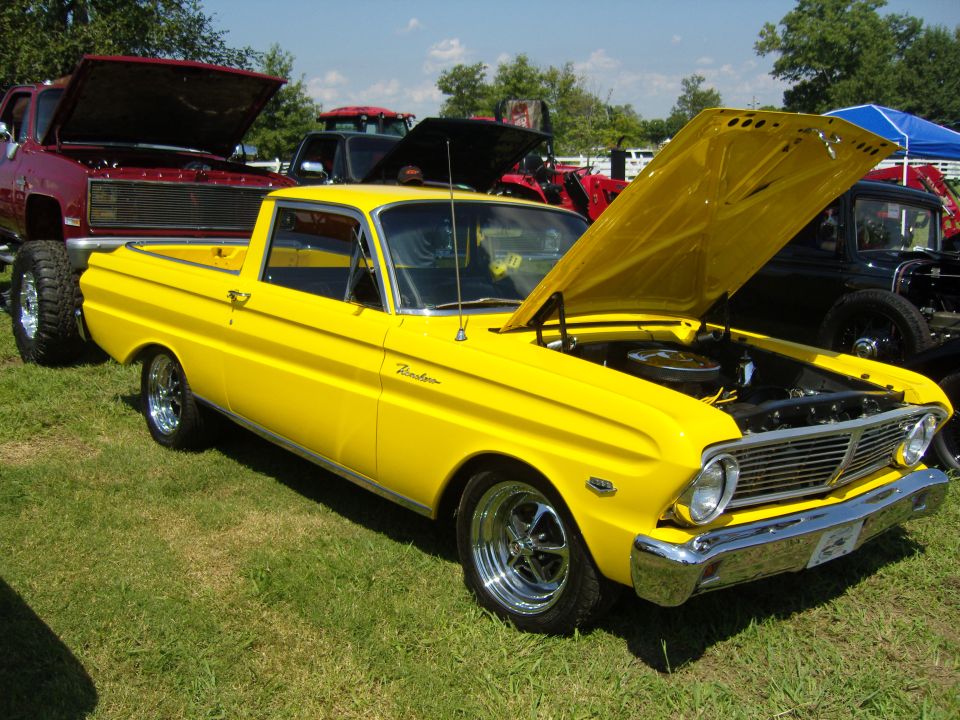 yellow pickup truck with hood open, parked on grass with other vehicles around