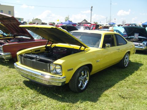 2007 Ford Mustang - A yellow 1975 Chevrolet Nova coupe is displayed with its hood open at an outdoor car show.
