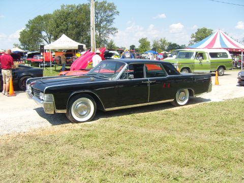 2007 Ford Mustang - A black 1965 Lincoln Continental is displayed at a car show, with tents and other cars visible.