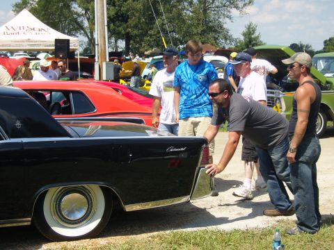 2007 Ford Mustang - A group of people inspect a classic black car at an outdoor event.