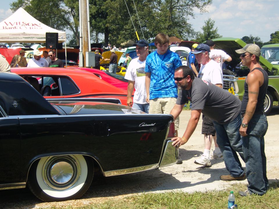 Black car's rear quarter panel and whitewall tire, with people gathered around