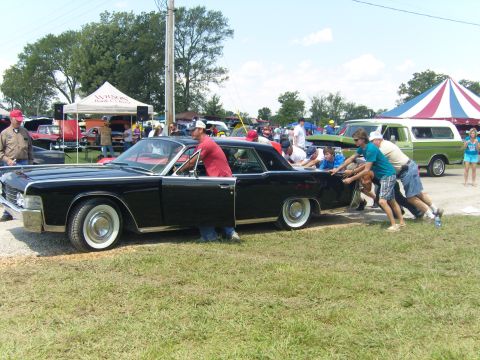 2007 Ford Mustang - Several people push a black Lincoln Continental at an outdoor car show.
