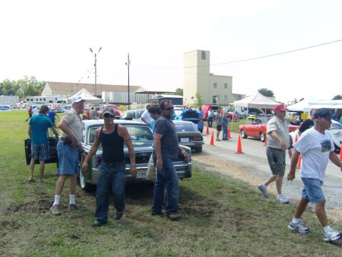 2007 Ford Mustang - A car show event with multiple vehicles and attendees under a cloudy sky.