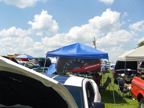 2007 Ford Mustang - An outdoor car show features multiple vehicles and tents under a partly cloudy sky.