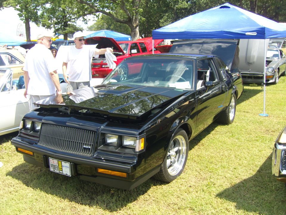 Black coupe with hood open, showing a large grille and custom wheels. License plate visible