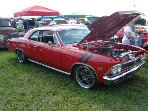 2007 Ford Mustang - A red classic car with racing stripes is displayed with its hood open at an outdoor car show.