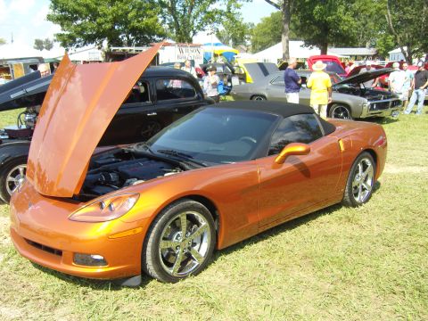 2007 Ford Mustang - An orange convertible sports car is displayed with its hood open at an outdoor car show.