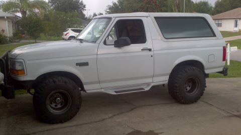 1995 Ford Bronco - A white Ford Bronco is parked on a driveway, showing its side profile and lifted suspension.