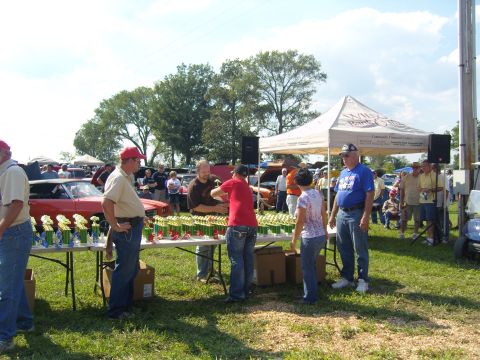 2007 Ford Mustang - People gather around a table laden with trophies at an outdoor event, with cars visible in the background.