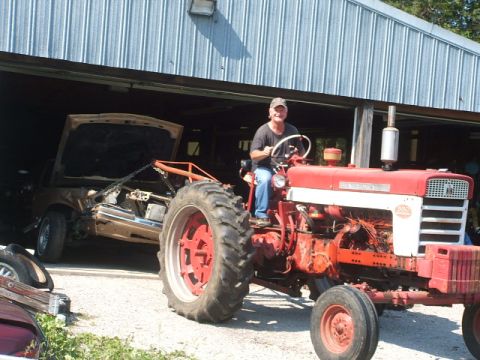 1966 Ford Ranchero - Tractor towing a car chassis under a metal roof structure.