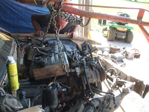 1966 Ford Ranchero - A vehicle's engine bay is being worked on, with a chain hoist overhead and a lawn tractor visible in the background.