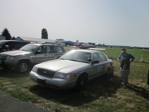 1991 Ford LTD Crown Victoria - A silver sedan is parked next to a Jeep Grand Cherokee with people standing nearby on a sunny day.