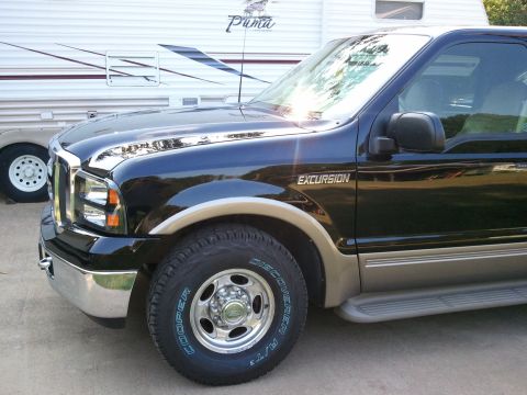 2001 Ford Excursion - The front quarter panel of a dark-colored Ford Excursion is visible, parked next to a travel trailer.