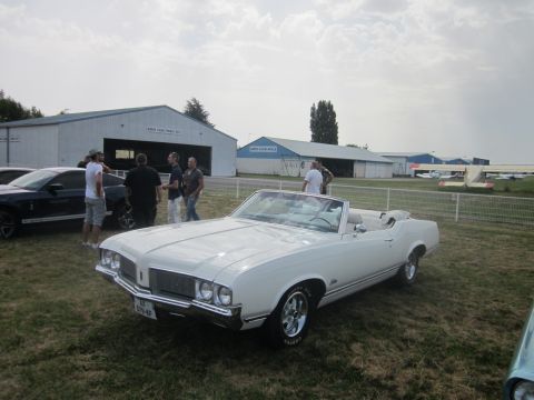 1991 Ford LTD Crown Victoria - A white convertible is parked on the grass in front of some hangars, with other cars and planes visible.