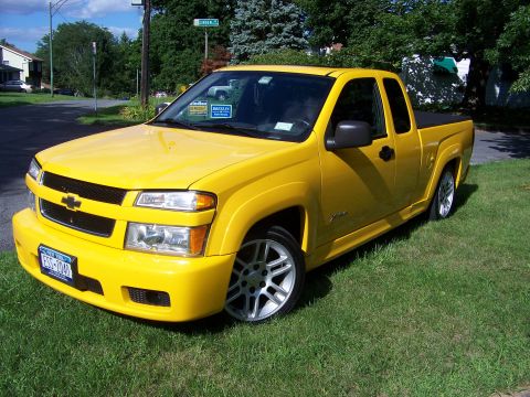 2005 Chevrolet Colorado - A yellow pickup truck with a custom body kit and aftermarket wheels is parked on a grassy lawn.