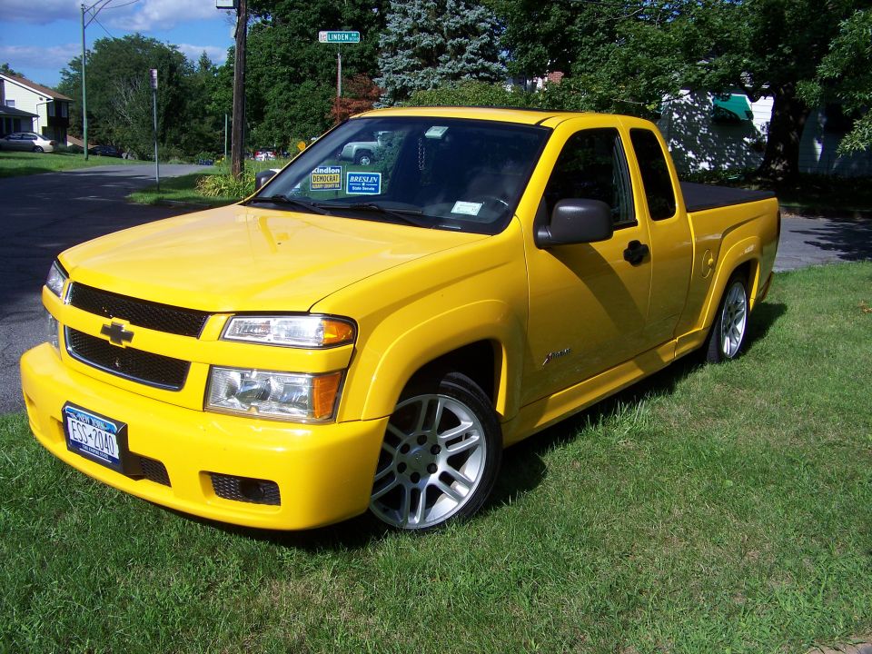 Yellow pickup truck with custom wheels and body kit, parked on grass