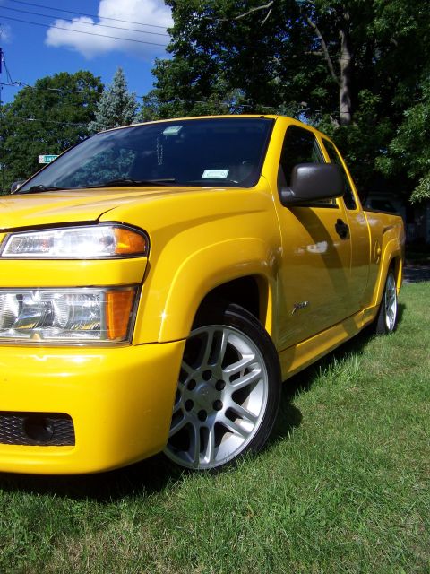 2005 Chevrolet Colorado - Yellow pickup truck with custom body kit and wheels parked on a grassy area under a blue sky with clouds.