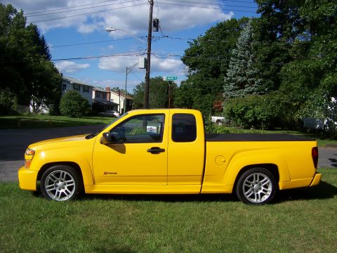 2005 Chevrolet Colorado - This yellow pickup truck is parked on a grassy area with houses and trees in the background.